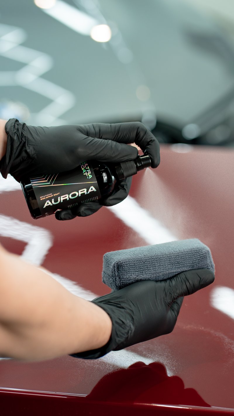 ULTRACOAT Aurora InteliGraph quick-spray ceramic held by a gloved hand spraying onto a red car bonnet, applicator pad ready