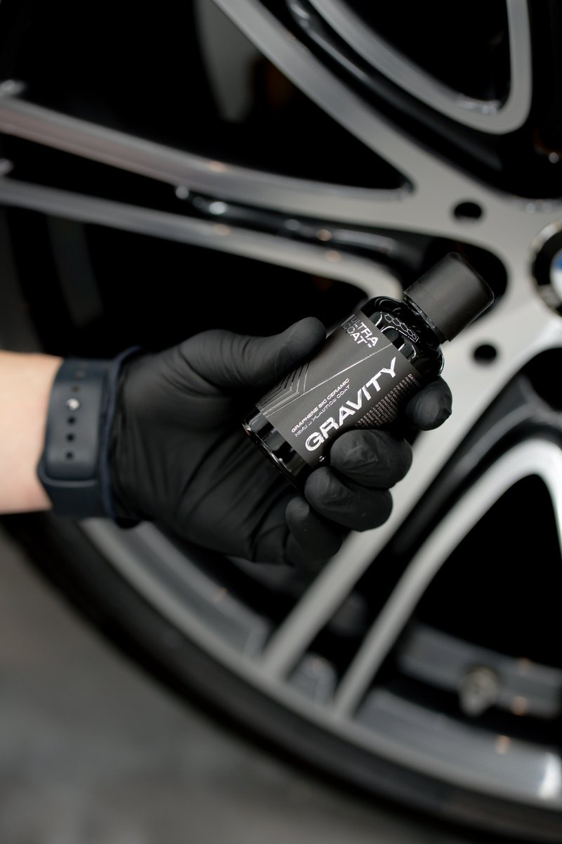 ULTRACOAT Gravity InteliGraph graphene-ceramic wheel coating held by a gloved hand against a BMW alloy wheel