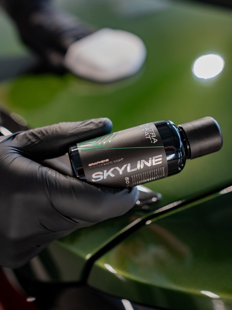 ULTRACOAT Skyline InteliGraph graphene-ceramic paint coat held by a gloved hand on a dark green car bonnet