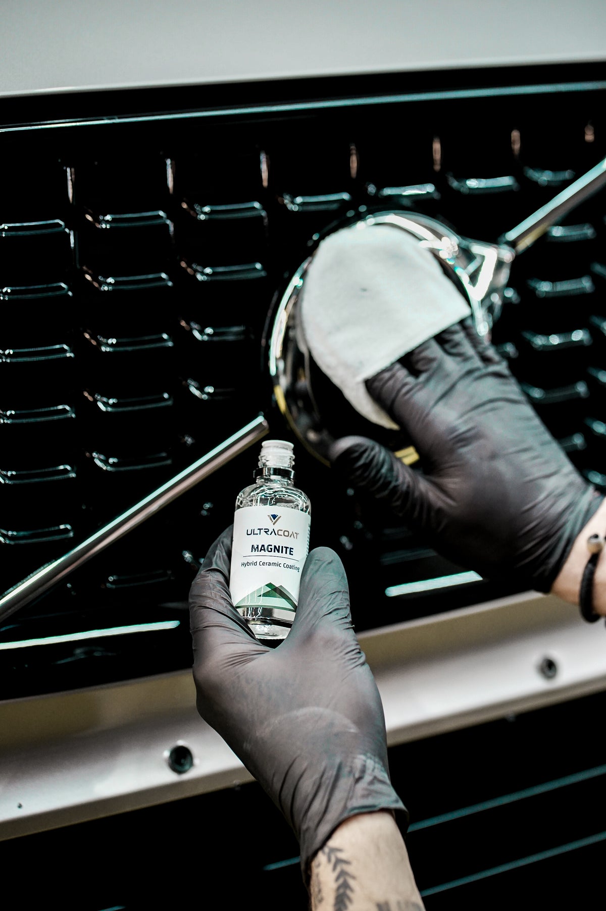 Applying Ultracoat Magnite to a chrome front grille badge with a cloth-wrapped applicator