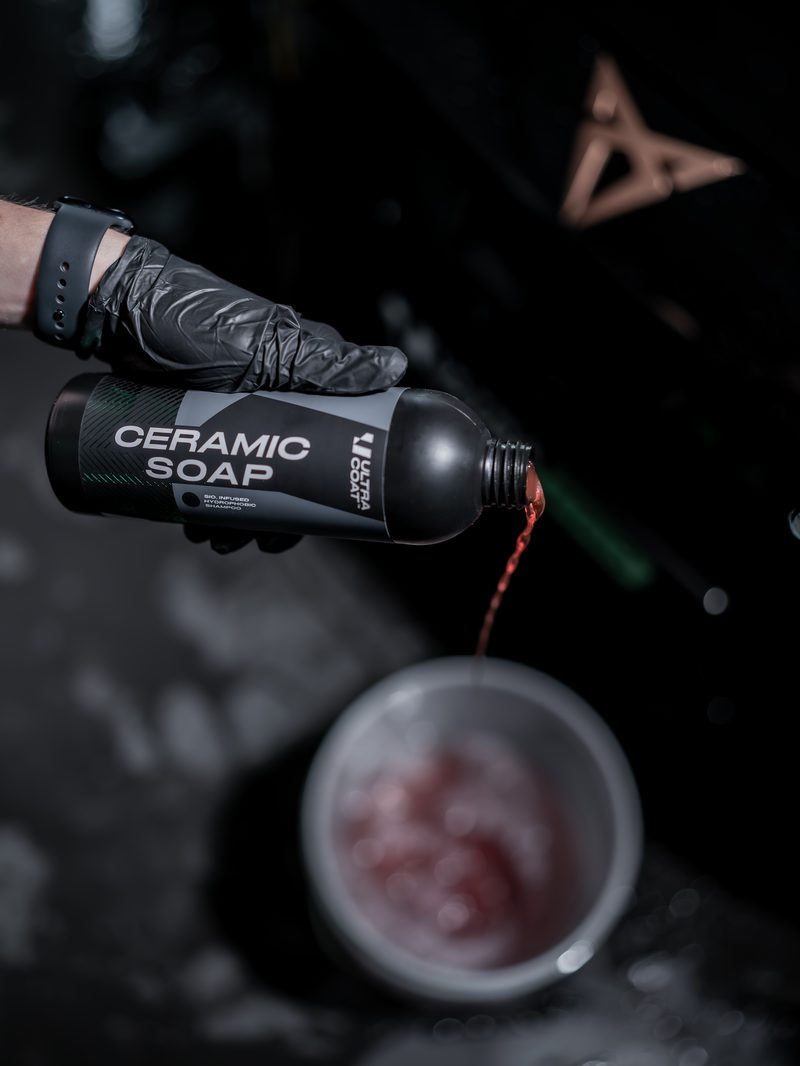 Detailer in black gloves pouring Ultracoat Ceramic Soap into a wash bucket