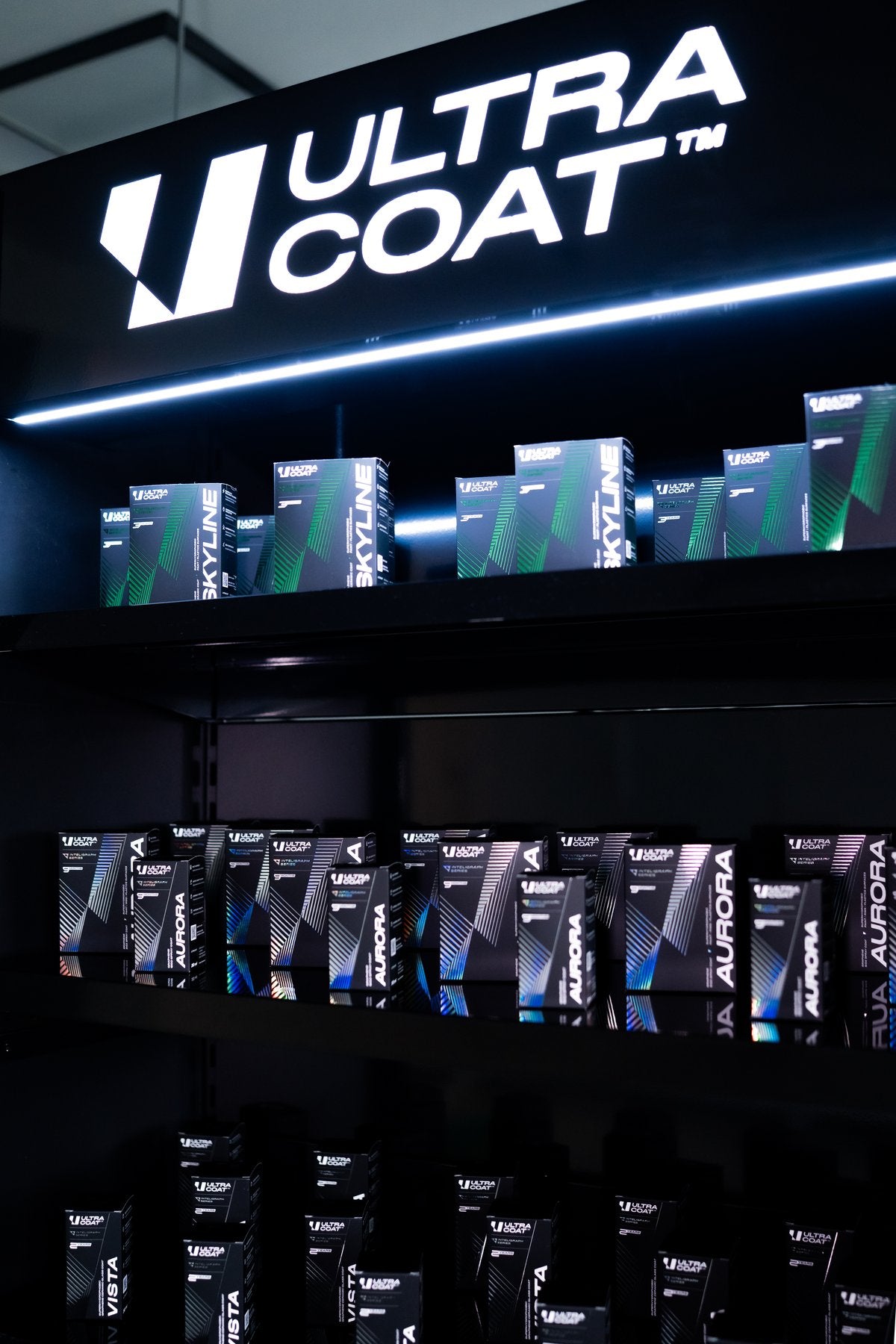 ULTRACOAT InteliGraph showroom stand — backlit brand marque with Skyline, Aurora, Vista and Gravity boxes on lit shelves