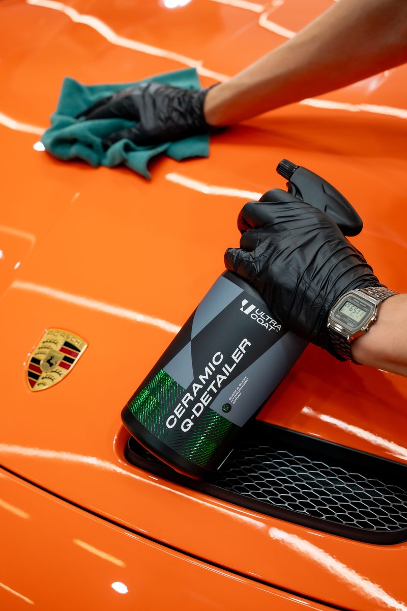 Detailer in black gloves spraying Ultracoat Ceramic Quick Detailer on an orange Porsche bonnet